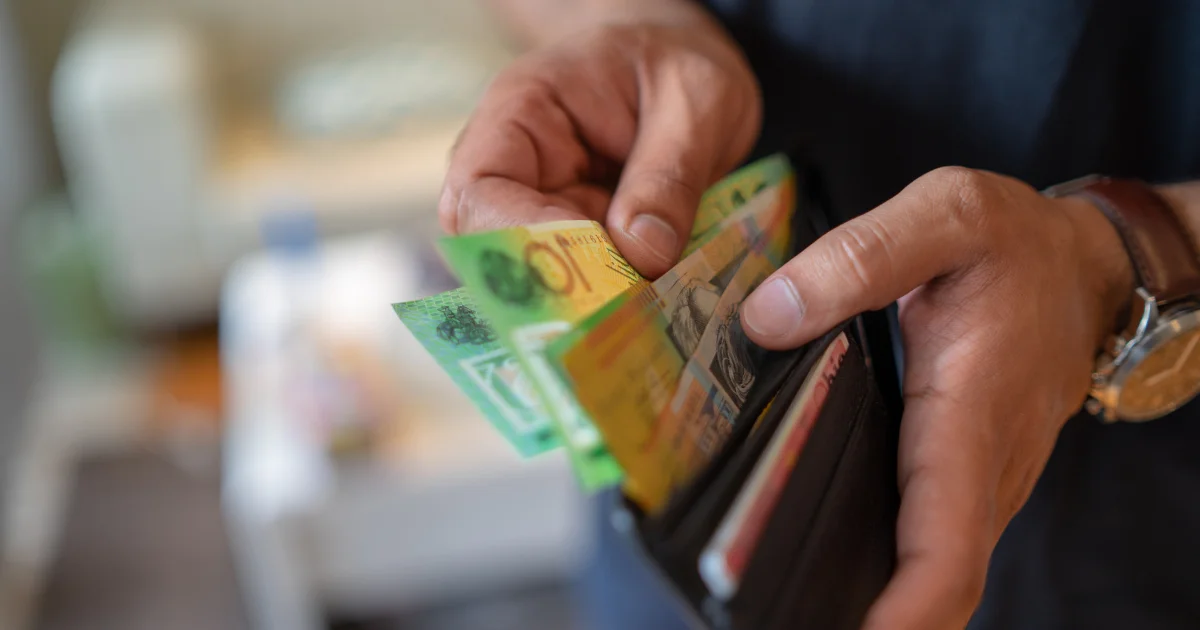 A close-up of hands opening a black leather wallet to reveal several colorful Australian dollar polymer banknotes, including fifty and ten-dollar bills.