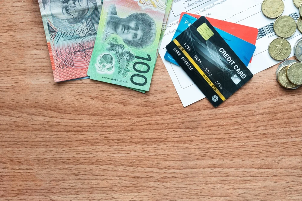 Australian currency, credit cards, and utility bills on a wooden surface