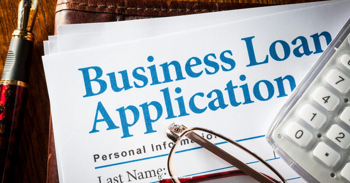 A close-up view of a 'Business Loan Application' document on a desk, topped with a fountain pen, reading glasses, and a calculator.
