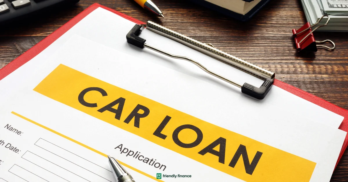 A clipboard holding a form with the large bold heading 'CAR LOAN' sits on a wooden desk next to a pen and other office supplies.