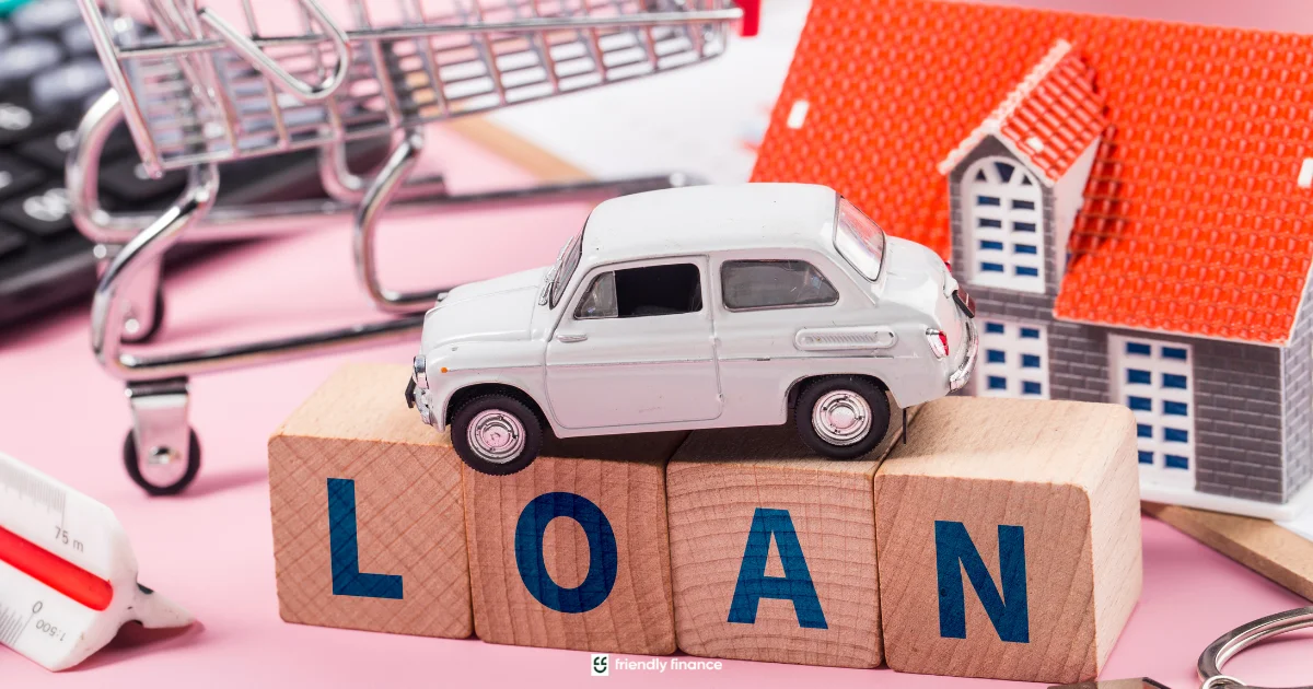 Wooden blocks spelling out 'LOAN', with a small toy car and a model house placed nearby to represent assets like a car or home used as collateral.