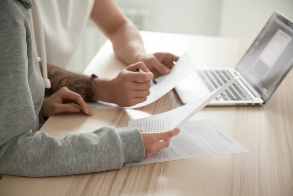 Two people reviewing documents together at a desk with a laptop open in front of them