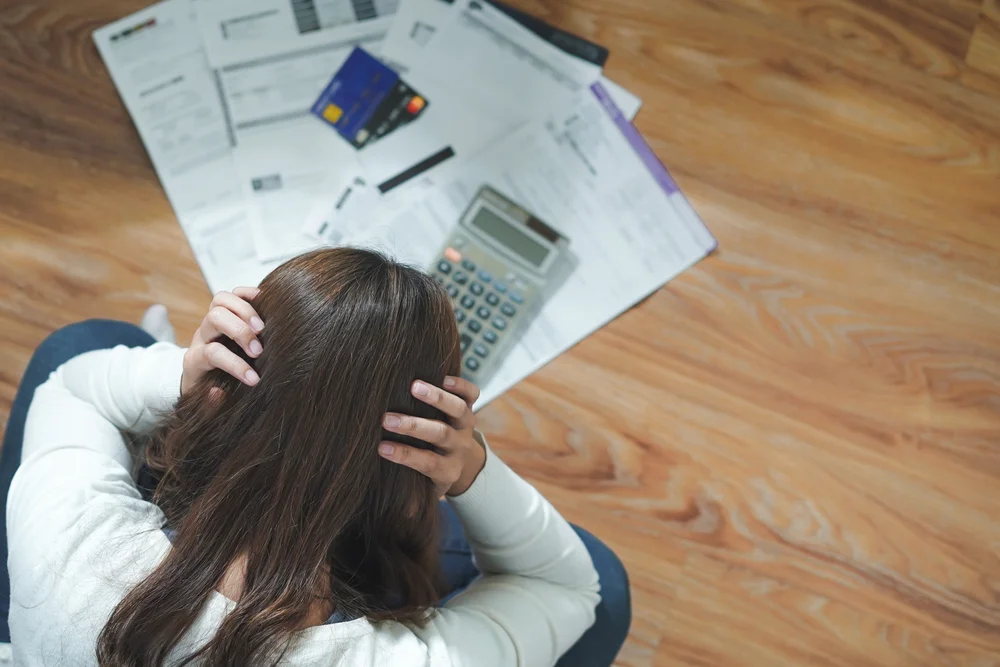 Woman sitting on floor stressed over unpaid bills, calculator, and credit cards