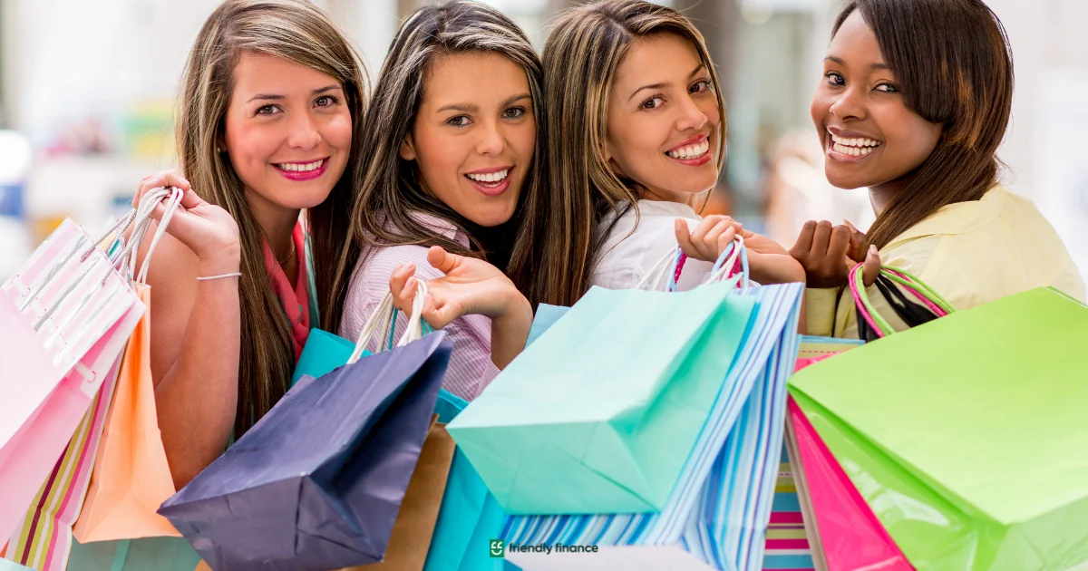 A group of four happy women look at the camera, holding many colorful shopping bags.