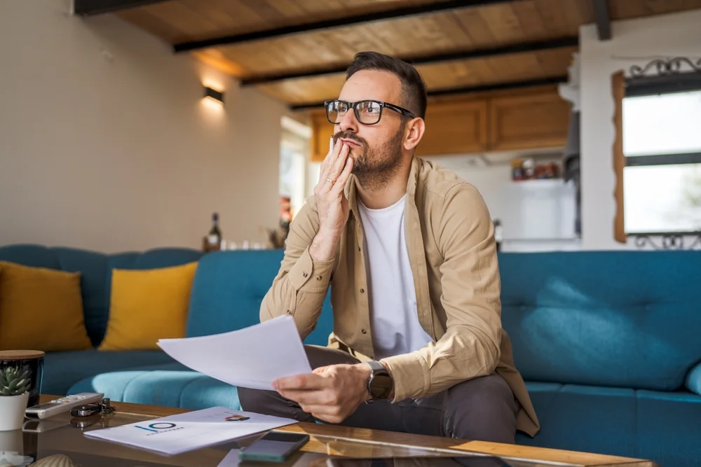 Man sitting on couch reviewing documents with a thoughtful expression