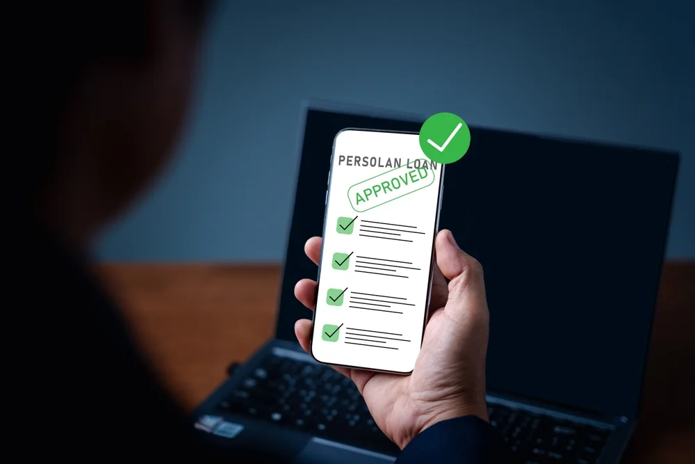 Hand holding phone showing personal loan approval screen with checklist and green ticks