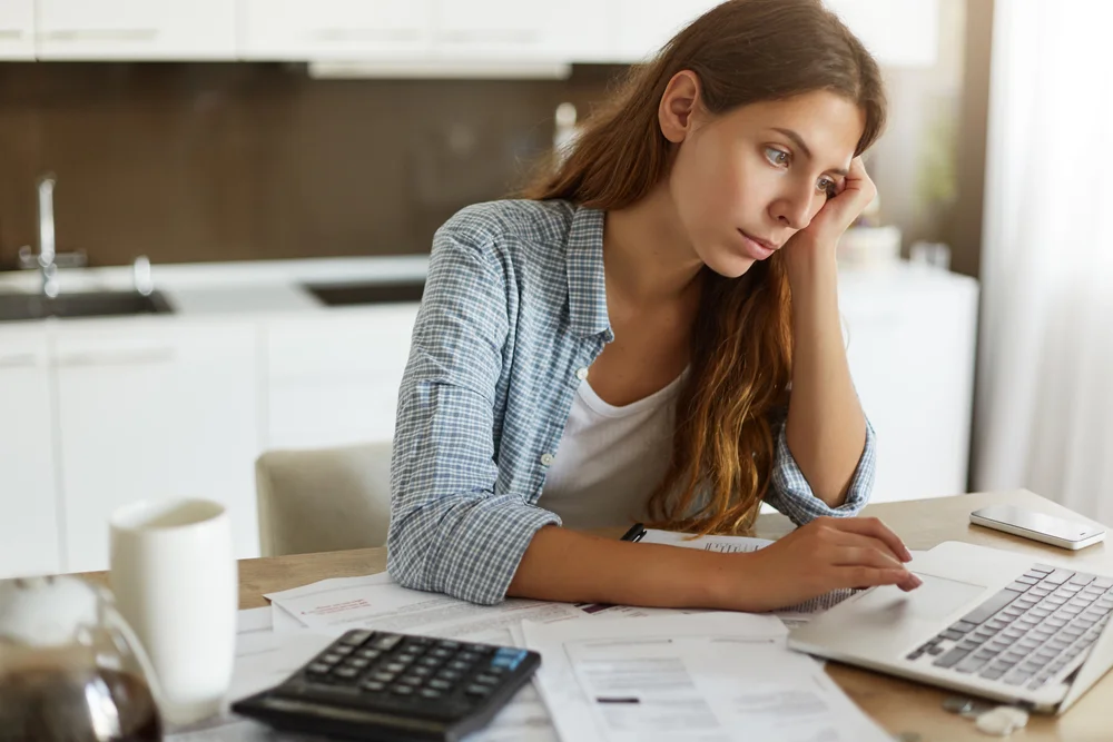 Stressed woman managing bills with laptop and calculator