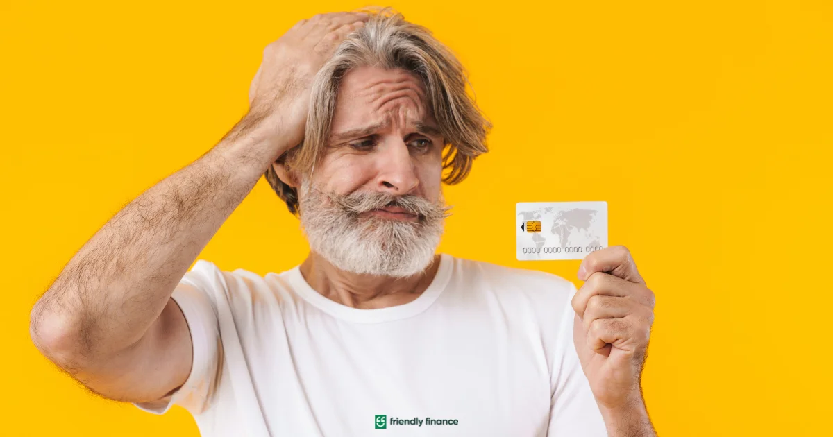 Worried man holding a credit card against yellow background, showing financial stress